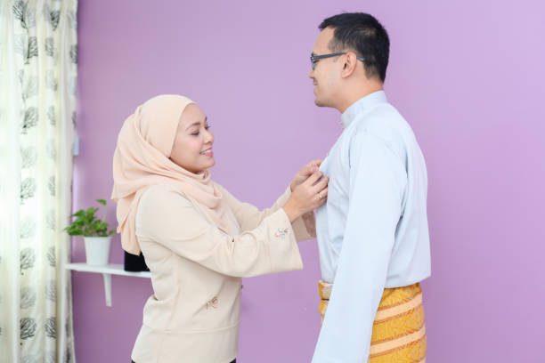 A Wife Helping Her Husband Wearing a Malay Traditional Clothing A Malay Muslim wife helping her husband wearing the traditional Malay clothing on Hari Raya Aidilfitri / Eid-Ul-Fitr in Malaysia. malay couple stock pictures, royalty-free photos & images