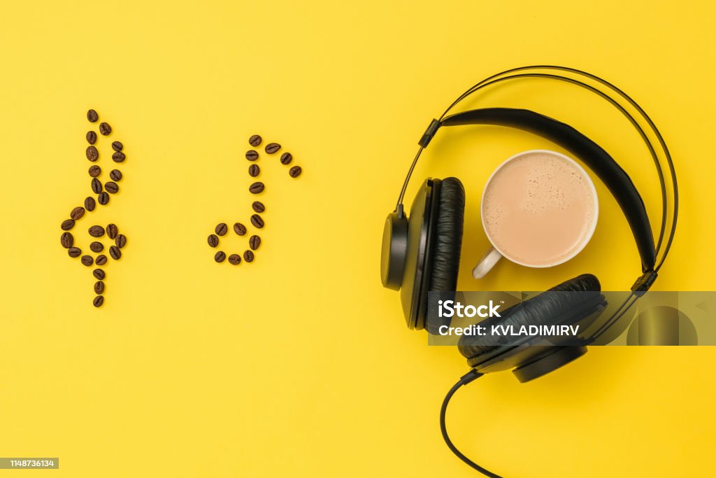Notes of coffee beans, headphones and a Cup of coffee on a yellow background. The concept of writing music. The view from the top. Notes of coffee beans, headphones and a Cup of coffee on a yellow background. The concept of writing music. Equipment for recording music tracks. The view from the top. Flat lay. Acoustic Music Stock Photo