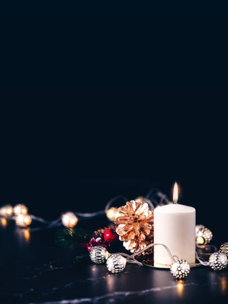 istock Christmas white candle with golden pine cone,mistletoe and light string glowing on black marble table with dark background.vertical banner holiday greeting card 1148743573