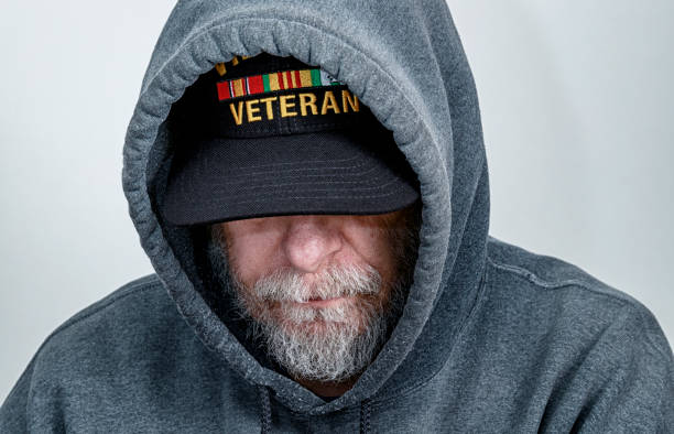 Vietnam War USA Military Veteran Wearing Hoody Looking Down A Vietnam War USA military veteran is looking down with his partially obscured face showing a serious facial expression. Though this shot is posed, this is a real life, real person Vietnam war veteran who's recently had some significant health issues. He is wearing an inexpensive, non-branded, generic, souvenir shop replica Vietnam veteran commemorative baseball hat style cap under his hoody sweatshirt hood. post traumatic stress disorder photos stock pictures, royalty-free photos & images