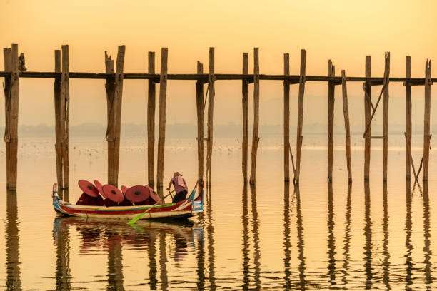 Burmese boatman and buddhist novice sitting in boat, Burmese boatman and buddhist novice sitting in boat, morning sunset in U Bein bridge, Mandalay, Myanmar mandalay photos stock pictures, royalty-free photos & images