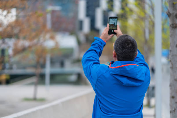 Middle aged man taking photos with his smart phone in the city.