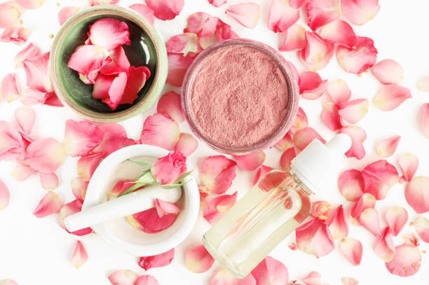 Top view botanical skincare home spa treatment with pink rose petals & clay face mask ose blossom, clay skin care mask, bottle of essential oil botanical spa treatment stock pictures, royalty-free photos & images