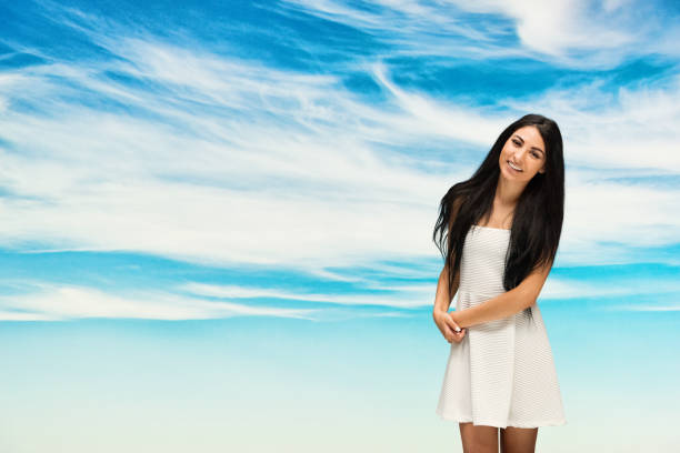 Elegant and expressive woman captured outdoors against a vibrant blue sky. Her confident gesturing and focused demeanor reflect emotion and energy. Ideal image for themes of femininity, expression, or natural beauty.