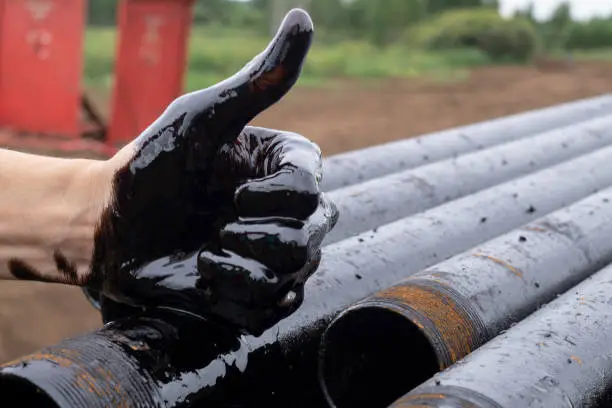 oil leaking. Very dirty hand.Stain hands showing thumbs up with black oil on drill pipes background. hand showing OK.