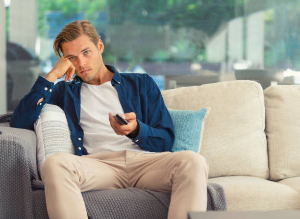 homme s’asseyant sur le sofa regardant la télévision. - television boredom men sofa photos et images de collection