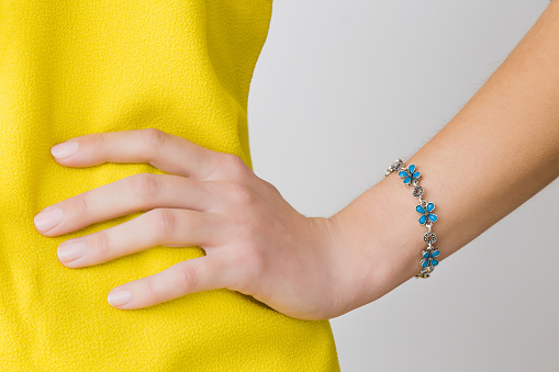 Woman in yellow, bright clothes on gray background. Hand on hips. Blue flower bracelet on wrist. Daily beauty. Part of body. Closeup. Front view.