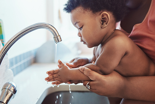 Shot of a mother helping her baby girl wash her hands in the bathroom sink