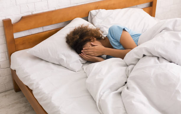 Girl covering face with hands, lying in bed