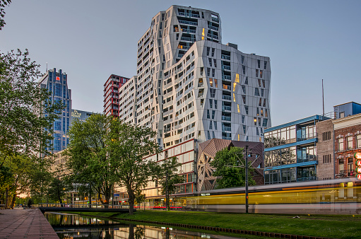 Rotterdam, The Netherlands, May 12, 2019: view of the green bank of Westersingel canal shortly before nightfall with a passing tram and the Calypso apartment building