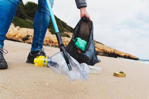 closeup of a caucasian man collecting garbage with a trash grabber stick, on a lonely beach, as an action to clean the natural environment
