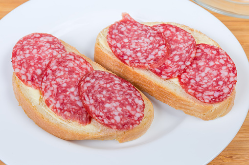 Two open sandwiches made with salami, wheat bread and butter on white dish close-up