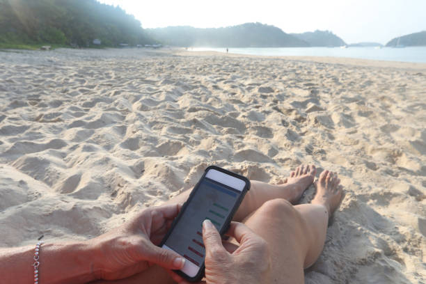 istock Woman uses phone while sitting on beach 1148793354