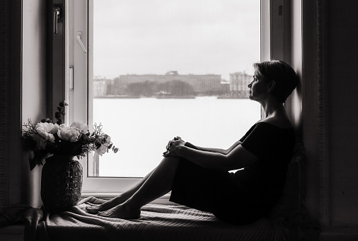 A woman is sitting on the windowsill and looking at the street