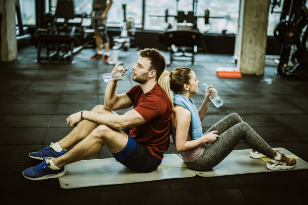Young athletic couple resting back to back on water break in a gym.