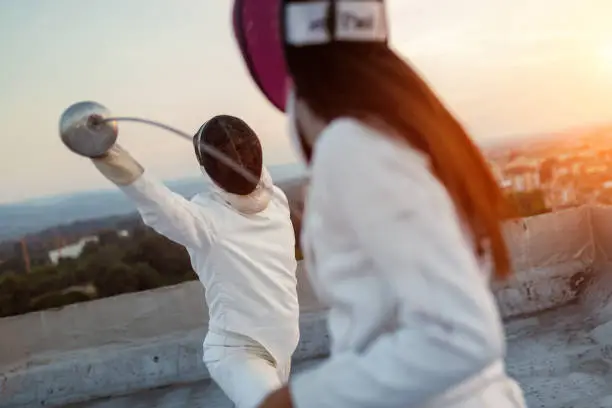 Photo of Two fencing athletes people fight on rooftop outdoors