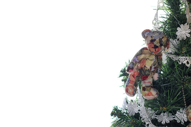Cute little boy in a blue cozy robe, pajamas and a Santa Clause hat is standing in front of a Christmas tree holding out a teddy bear toy he unwrapped for the holiday.