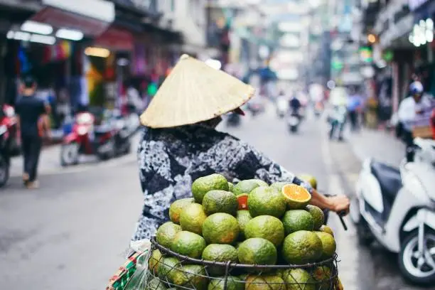 City life in street of old quarter in Hanoi. Fruit seller in traditional  conical hat. Selective focus on mandarin.