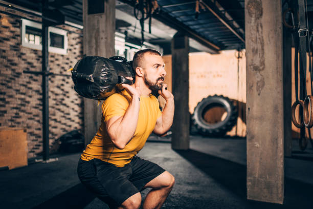 Muscular athlete doing core bag squats workout in a gym.