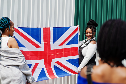 Two african american girls with Great Britain flag on hands, friends making photo on phone.