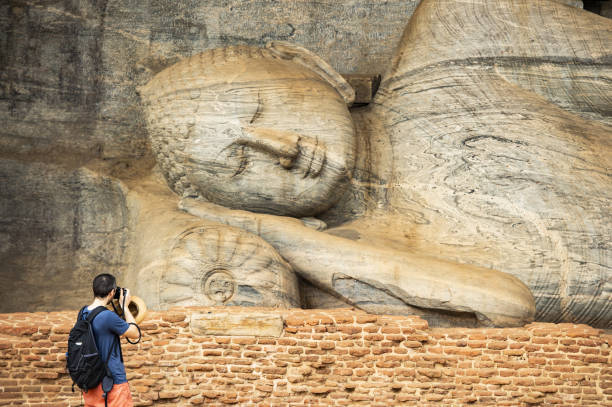un turista sta scattando foto alla bellissima statua del buddha sdraiato scolpita nella pietra. il gal vihara è un tempio rupe rock situato nell'antica città di polonnaruwa, nella provincia centro-settentrionale dello sri lanka. - reclining buddha foto e immagini stock