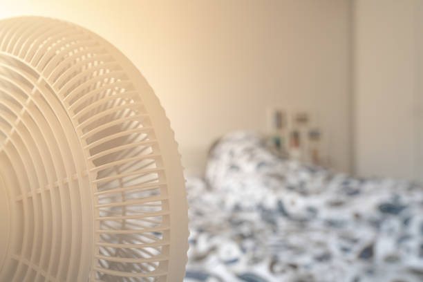 istock Person sleeping in bed with a fan blowing on hot summer day with bright light 1148802804