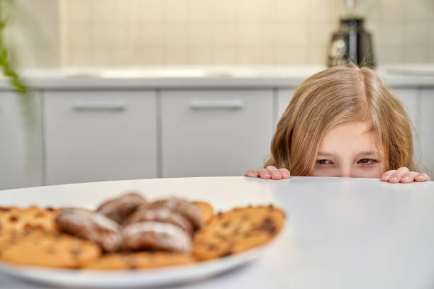 istock Girl hiding behind table at kitchen and looking at cookies 1148803949
