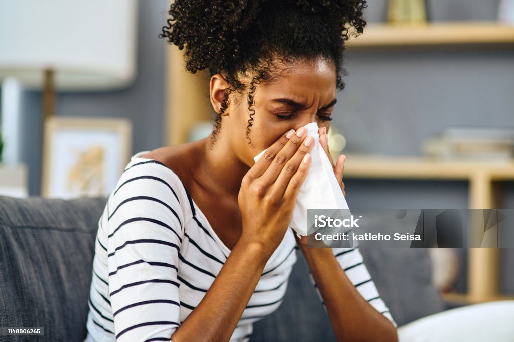 I'll have to stay in today Shot of a young woman blowing her nose with a tissue at home Sneezing Stock Photo