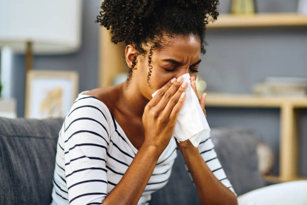 I'll have to stay in today Shot of a young woman blowing her nose with a tissue at home sneezing photos stock pictures, royalty-free photos & images