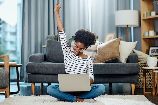 Shot of a young woman cheering while using her laptop at home