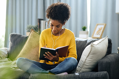 Shot of a young woman listening to music while writing in her notebook