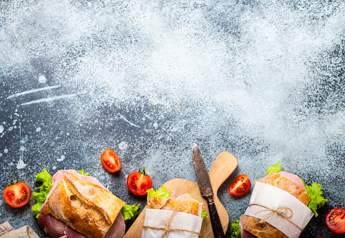 Fresh ciabatta sandwiches with ham, cheese, lettuce, tomatoes, stone concrete background, close-up, top view with space for text. Food template with making healthy sandwiches for snack or lunch