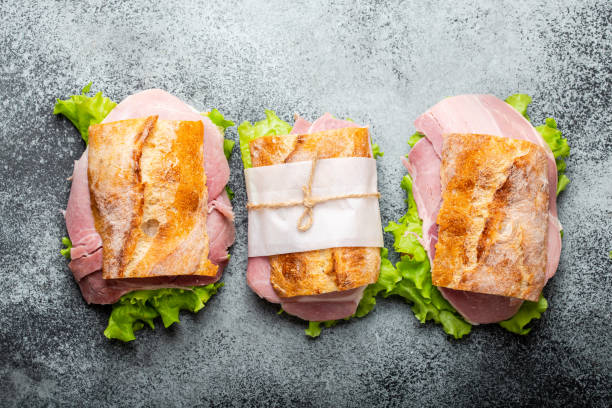 Fresh ciabatta sandwiches for lunch Fresh ciabatta sandwiches with ham, cheese, lettuce on stone concrete background, close-up, top view. Making healthy sandwiches for snack or lunch concept ciabatta stock pictures, royalty-free photos & images