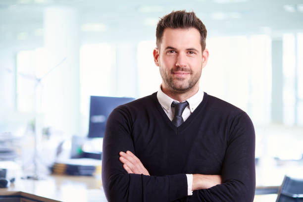 Casual businessman portrait while standing in the office with folded arms Portrait shot of handsome businessman wearing casual clothes while standing with arms crossed in the office. assistant stock pictures, royalty-free photos & images