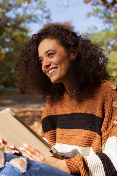 istock Beautiful young girl with dark curly hair using tablet computer, outdoor. 1148809026
