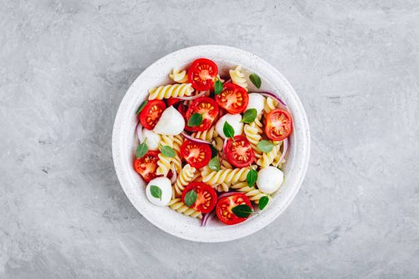 istock Italian pasta salad with tomatoes, mozzarella cheese, red onion and basil. Top view. 1148809351