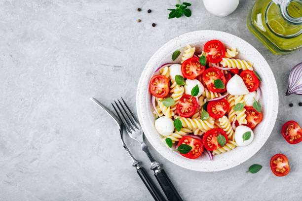 insalata di pasta italiana con pomodori, mozzarella, cipolla rossa e basilico. vista dall'alto. - fusilli foto e immagini stock