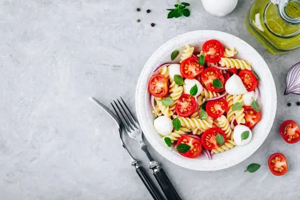 Italian pasta salad with tomatoes, mozzarella cheese, red onion and basil. Top view, copy space