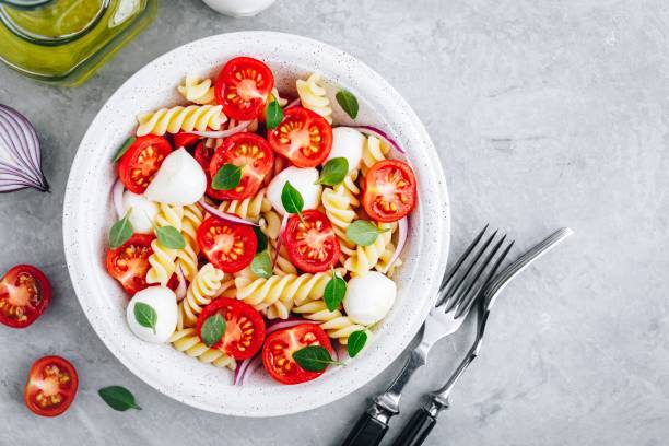 istock Italian pasta salad with tomatoes, mozzarella cheese, red onion and basil. Top view. 1148809414