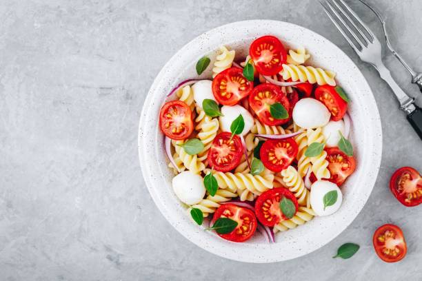 istock Italian pasta salad with tomatoes, mozzarella cheese, red onion and basil. Top view. 1148809457