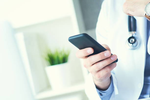 istock Male doctor in white coat is using a modern smartphone device with touch screen. Doctor hands with mobile phone. 1148822313