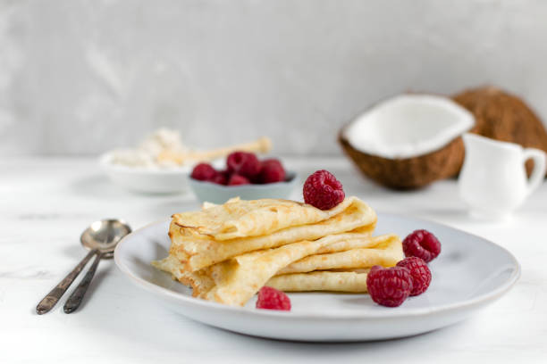 Morning, breakfast - traditional russian blini pancakes, french crepes served with fresh raspberries, coconut Morning, breakfast - traditional russian blini pancakes, french crepes served with fresh raspberries, coconut, white wooden table blini photos stock pictures, royalty-free photos & images