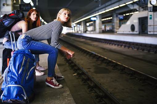 Young women sitting on their suitcases at railroad station, waiting on their train.