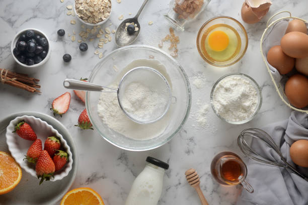 faire des crêpes, gâteau, cuisson des mains de boulanger versant ou tamisant la farine dans le bol. concept de la cuisson des ingrédients et la méthode sur fond de marbre blanc. recettes de desserts et fait maison. - saupoudreuse à farine photos et images de collection