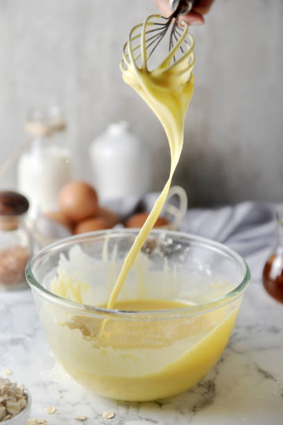 istock Making pancakes, cake, baking side view of baker hands pouring batter and whisking batter in bowl. Concept of Cooking ingredients and method on white marble background, Dessert recipes and homemade. 1148824329