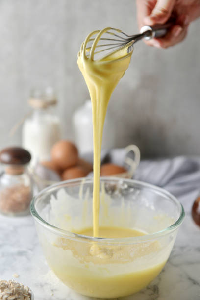 istock Making pancakes, cake, baking side view of baker hands pouring batter and whisking batter in bowl. Concept of Cooking ingredients and method on white marble background, Dessert recipes and homemade. 1148825225