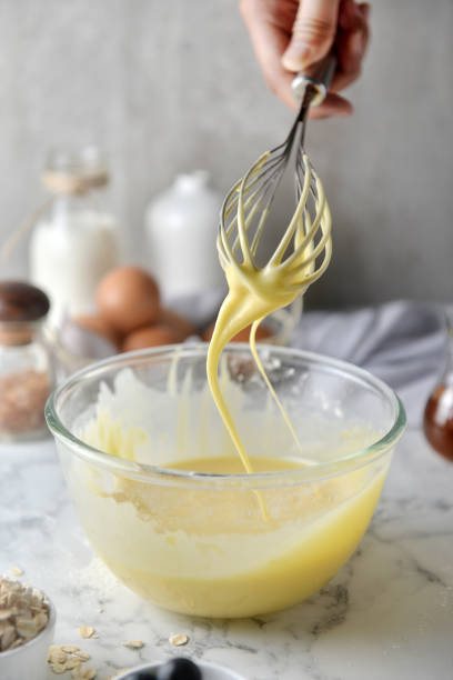 istock Making pancakes, cake, baking side view of baker hands pouring batter and whisking batter in bowl. Concept of Cooking ingredients and method on white marble background, Dessert recipes and homemade. 1148827532