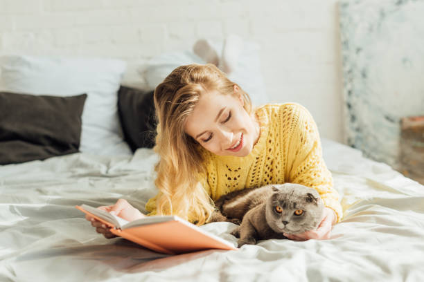 istock beautiful smiling young woman reading book while lying in bed with scottish fold cat 1148829085