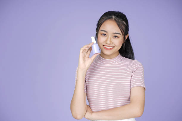 Asian young teenage beautiful cheerful girl hold skincare mockup blank product in pink shirt, on violet background Asian young teenage beautiful cheerful girl hold skincare mockup blank product in pink shirt, on violet background vietnamese girls for sale stock pictures, royalty-free photos & images