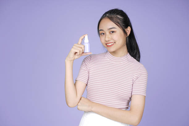 Asian young teenage beautiful cheerful girl hold skincare mockup blank product in pink shirt, on violet background Asian young teenage beautiful cheerful girl hold skincare mockup blank product in pink shirt, on violet background vietnamese girls for sale stock pictures, royalty-free photos & images